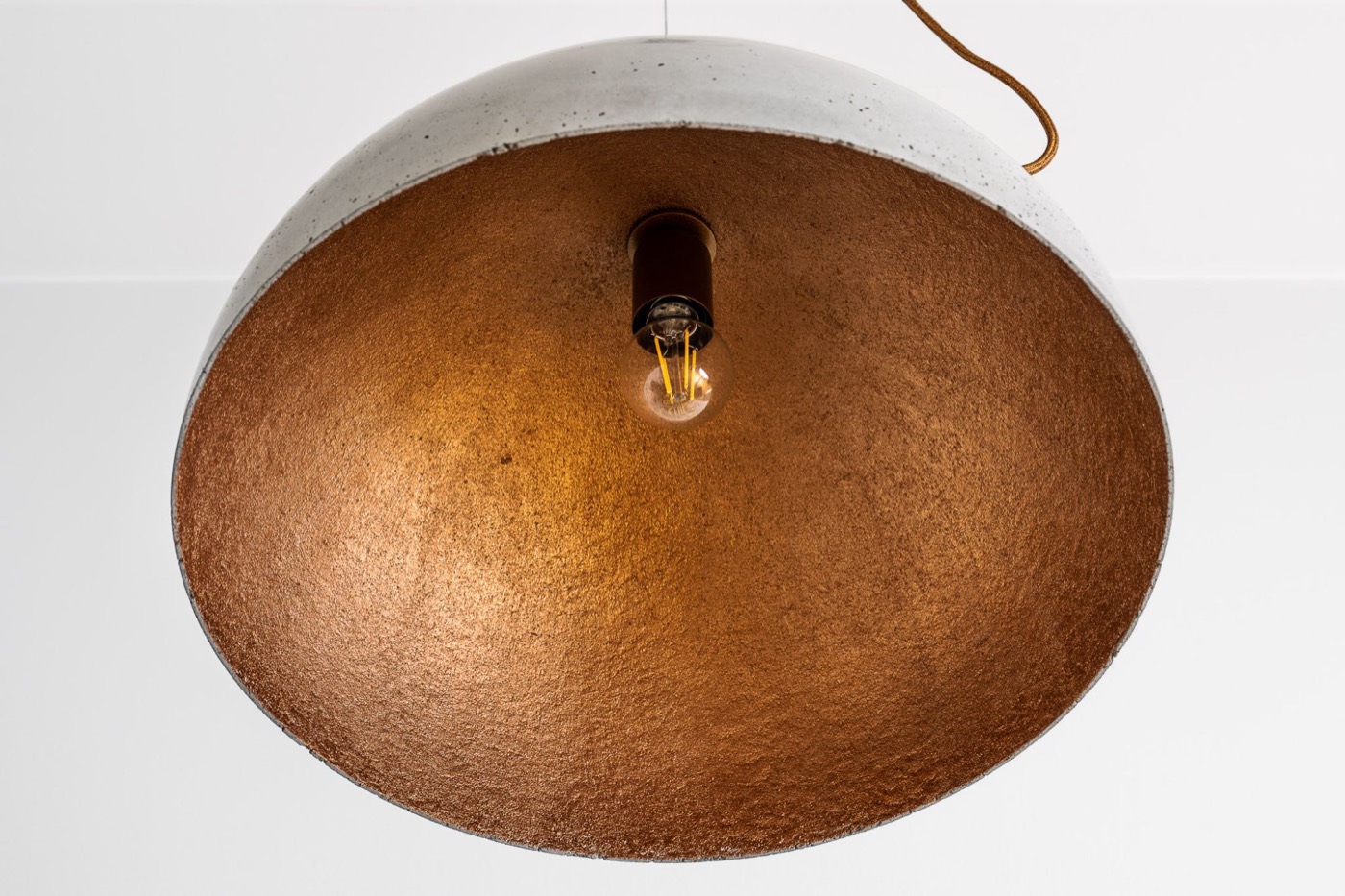 Inside a concrete hemisphere shade — a textured warm metallic finish around a filament bulb