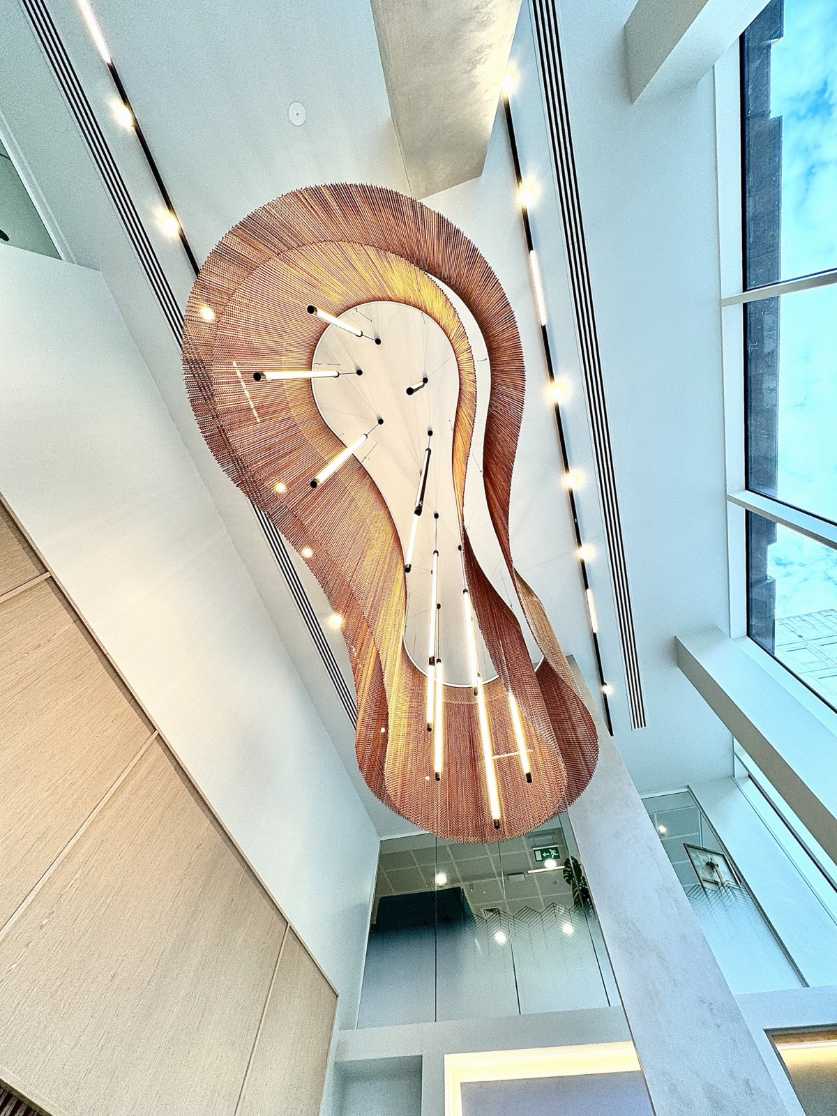7 Park Row — upward view of the sculptural copper centrepiece with Aqform Piper suspended luminaires in the double-height reception void