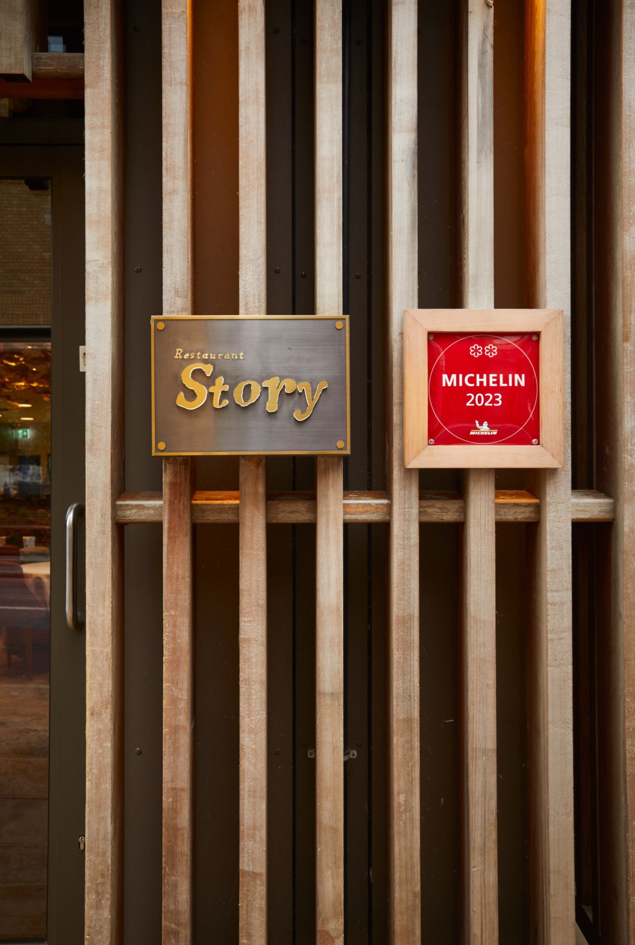 Restaurant Story entrance — Michelin plaque and timber slat facade with warm interior glow