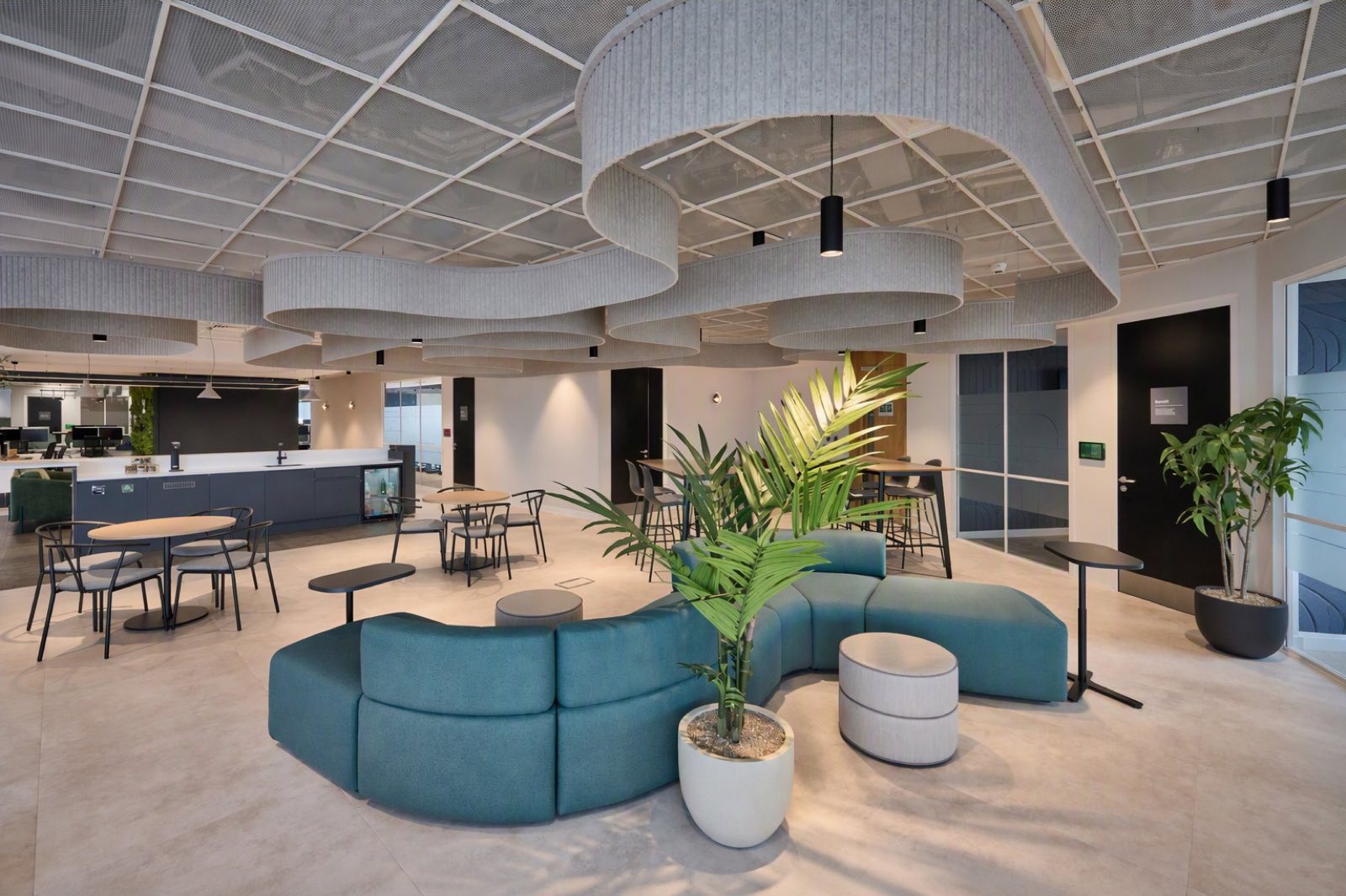 Breakout space with cloud-like acoustic rafts and black cylinder pendants over curved seating