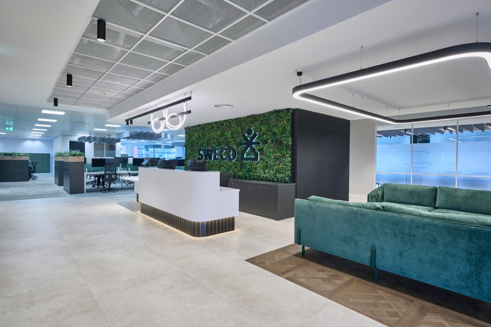 Sweco UK reception — Tubeflex loops on Aqform Multitrack above the desk, moss wall with Sweco branding and green velvet seating